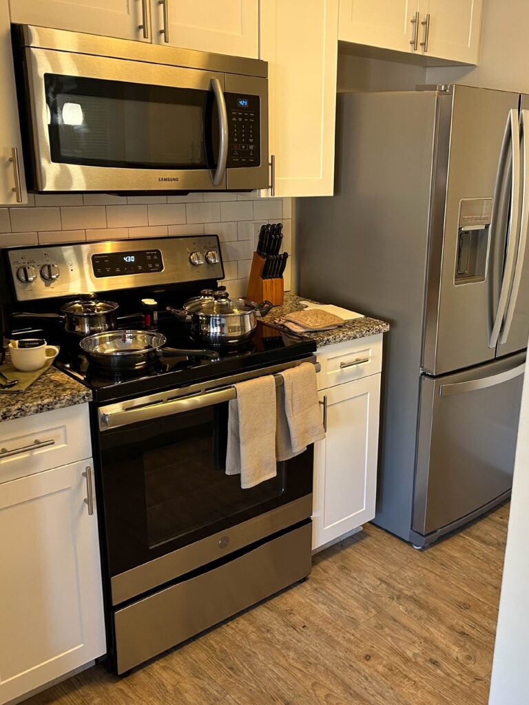 Modern kitchen at Vista Commons in Columbia, South Carolina, featuring stainless steel appliances, granite countertops, white cabinetry, subway tile backsplash, and a full-size refrigerator.