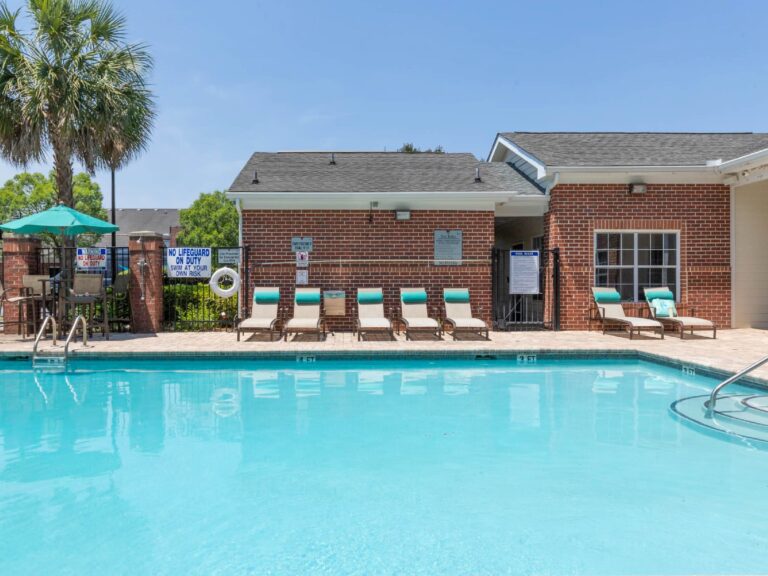 Resort style swimming pool at Vista Commons in Columbia, South Carolina, featuring turquoise water, poolside loungers, palm trees, and a spacious sun deck.