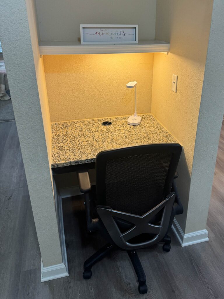 Built-in workspace nook at Waterstone at Brier Creek featuring a granite desktop, ergonomic office chair, task lighting, and convenient power access for remote work or studying.