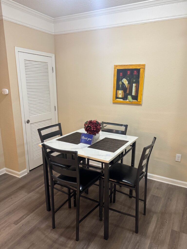 Dining area at Waterstone at Brier Creek featuring a modern four-person dining table with high-back chairs, decorative centerpiece, and convenient access to the kitchen and living spaces.