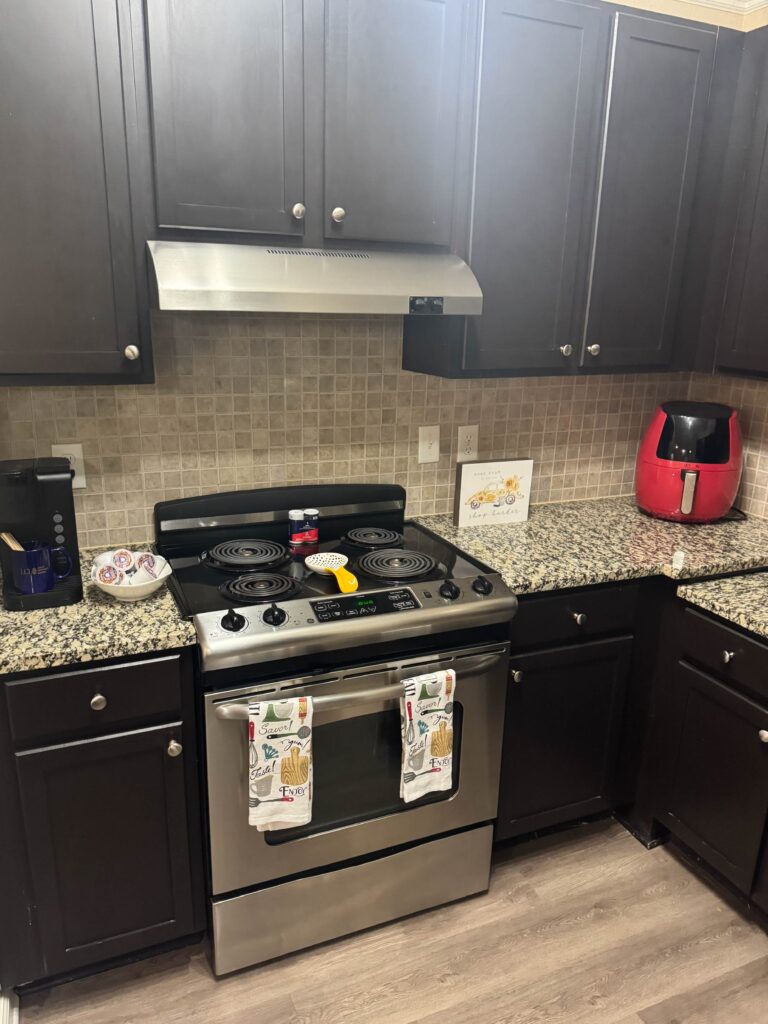 Modern kitchen at Waterstone at Brier Creek featuring granite countertops, stainless steel oven, full-size cooking range, coffee maker, air fryer, and extensive cabinet storage.