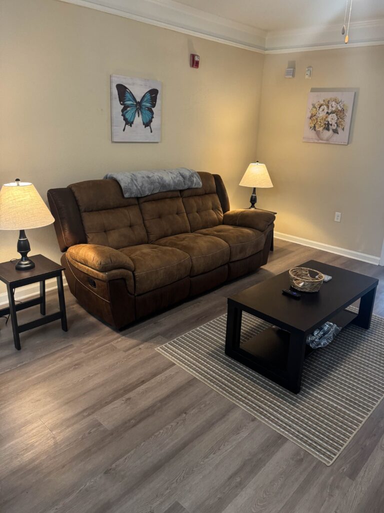 Inviting living room featuring a plush reclining sofa, coffee table, accent lighting, contemporary artwork, and luxury vinyl plank flooring at Waterstone at Brier Creek in Lexington, Kentucky.