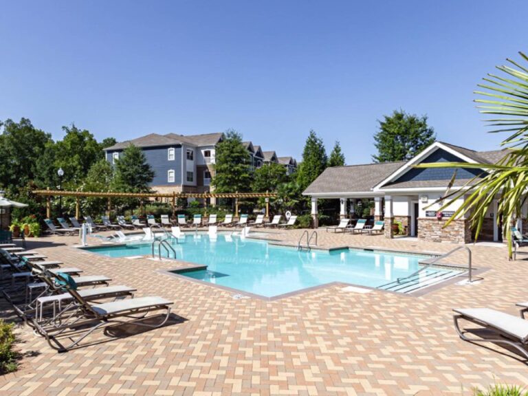 Resort style outdoor swimming pool surrounded by lounge chairs, sun deck seating, landscaped grounds, and a poolside clubhouse at Waterstone at Brier Creek in Lexington, Kentucky.