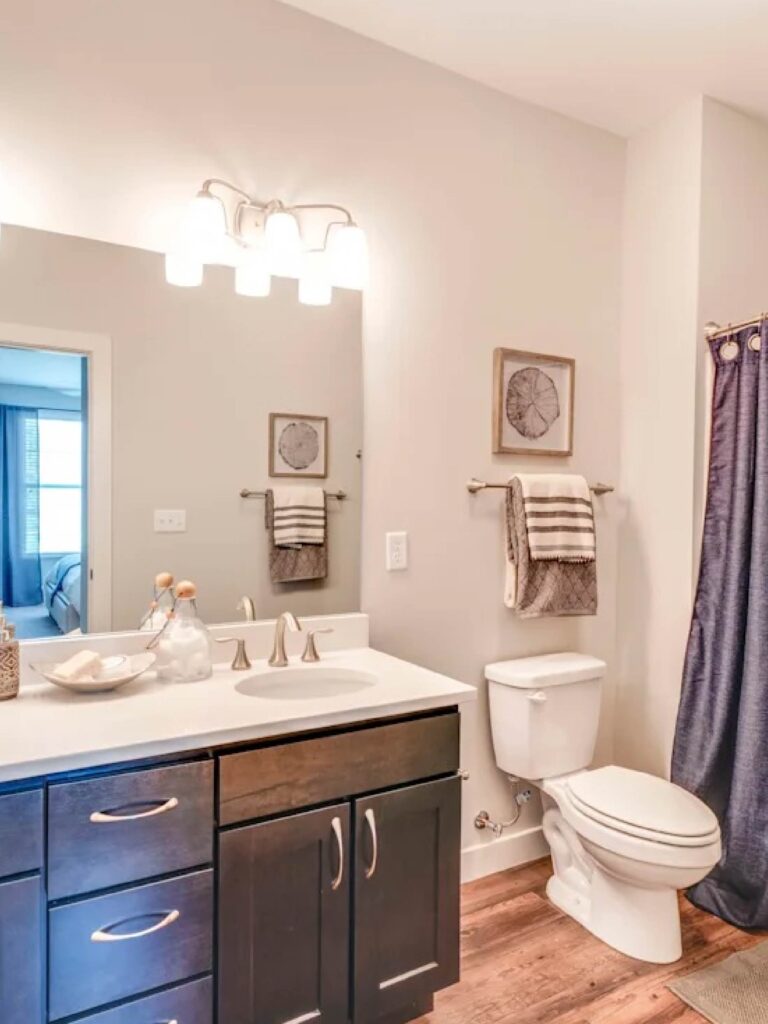 Modern apartment bathroom with dark wood cabinetry, white countertops, large mirror, and shower curtain.