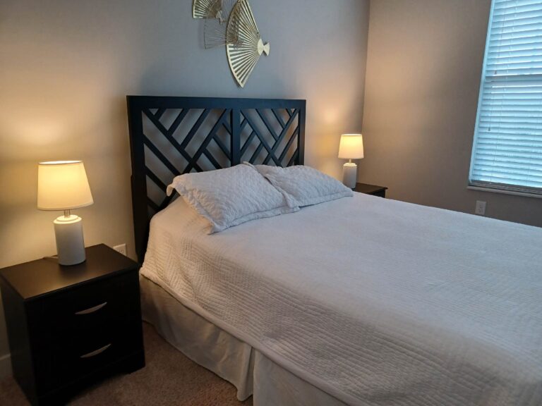 Modern furnished bedroom with a king-size bed, geometric headboard, bedside tables, and soft accent lighting.