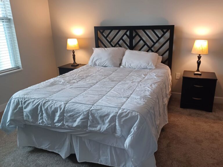 Furnished bedroom with a king size bed, geometric headboard, bedside tables, and warm lighting.