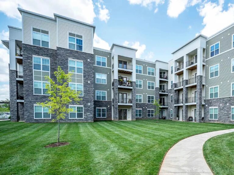 Modern apartment community exterior with landscaped green space, walking paths, balconies, and upscale architectural finishes.