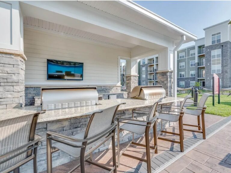Outdoor grilling pavilion with built-in grills, bar seating, mounted TV, and covered entertaining space.