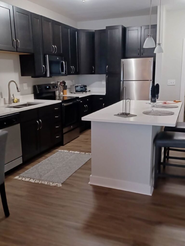 Modern apartment kitchen with dark cabinetry, stainless steel appliances, white countertops, and a center island with seating.