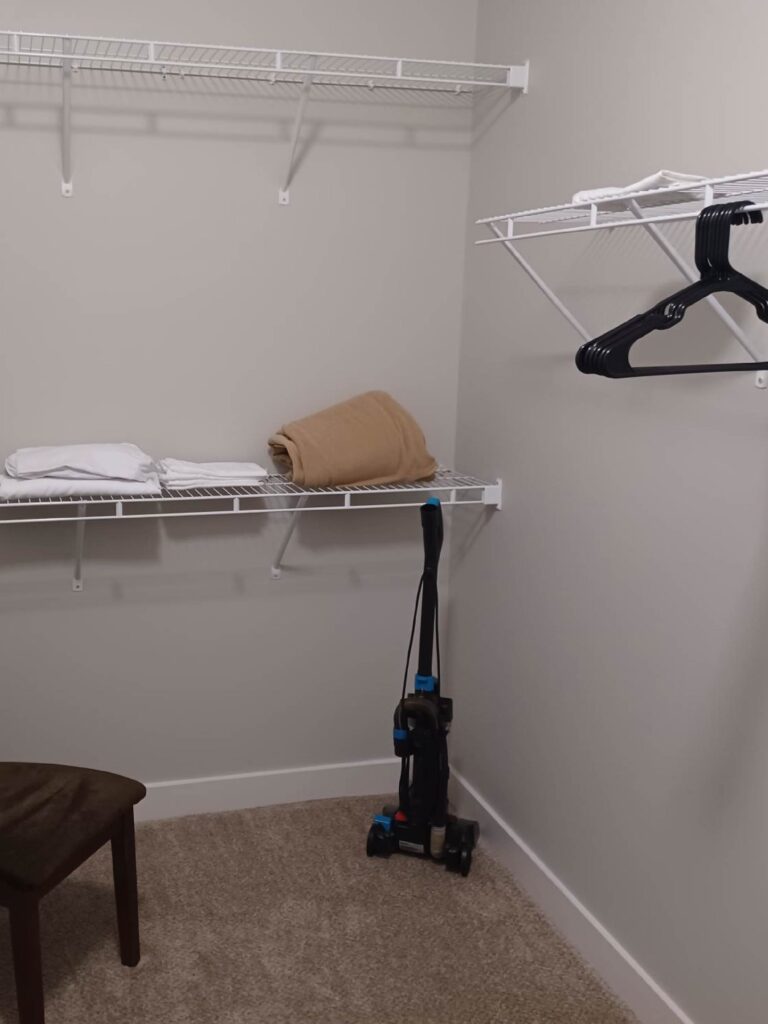 Spacious walk-in closet with wire shelving, carpet flooring, hangers, folded linens, and a vacuum.