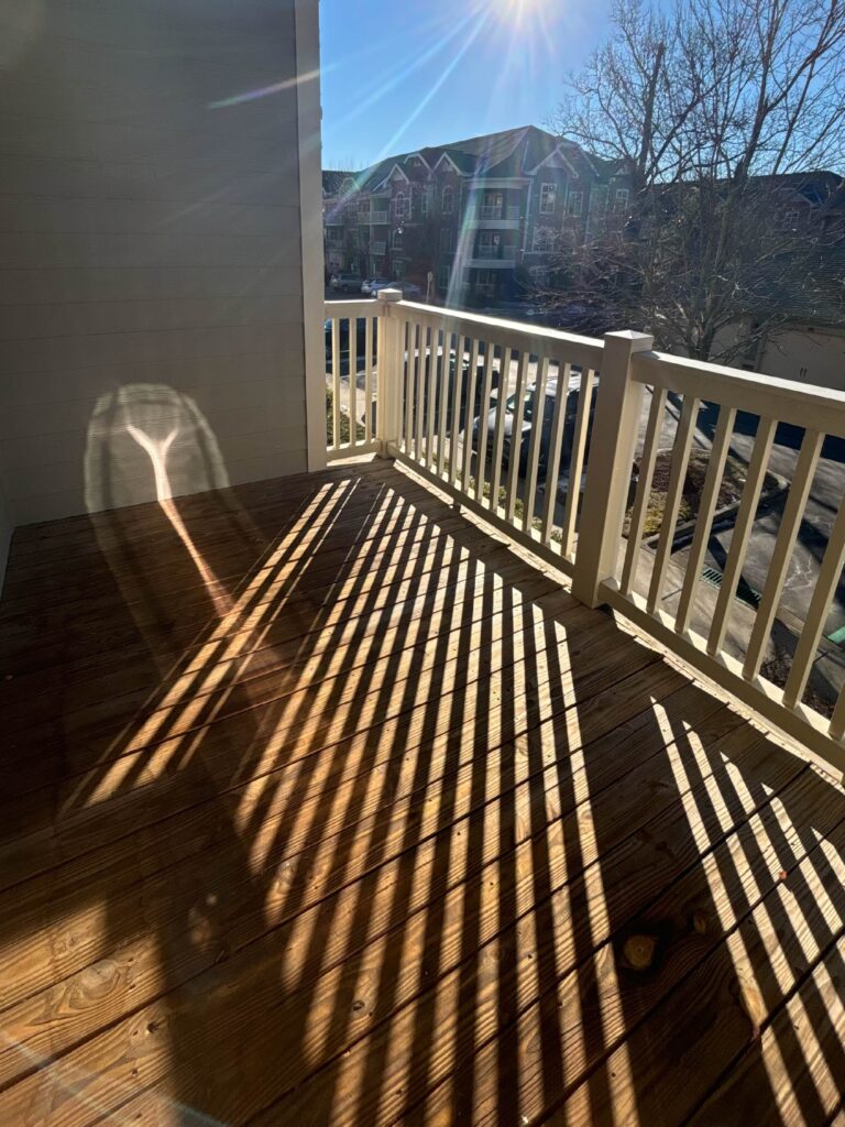 Private covered balcony with wood plank flooring and white railing, overlooking the Weirbridge Village community and surrounding Asheville neighborhood.