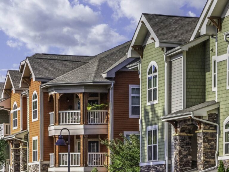 Exterior view of Weirbridge Village featuring Craftsman-style architecture with colorful siding, stone accents, covered balconies, and landscaped grounds set against the Blue Ridge Mountain backdrop.