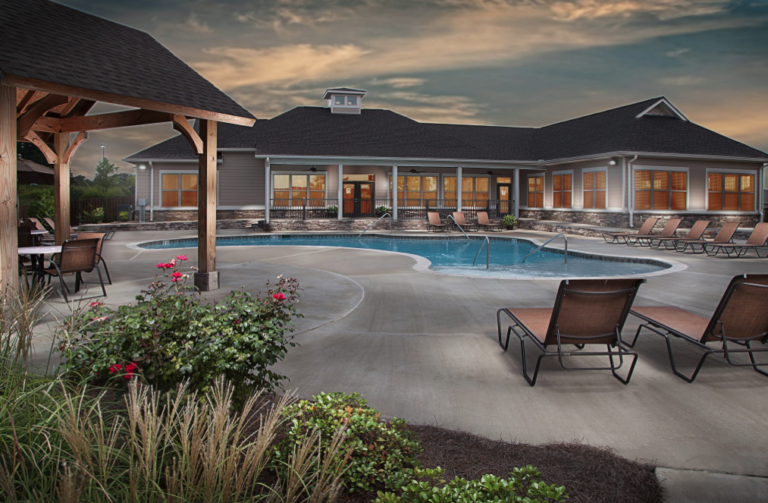 Resort style community swimming pool with sundeck seating, covered gathering area, and landscaped surroundings at Mill at McCullough Apartments in Tupelo, Mississippi.