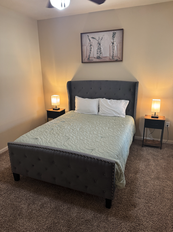 Primary bedroom with upholstered queen bed and bedside lighting in a fully furnished corporate housing apartment at Vista Ridge