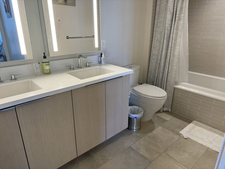 Modern bathroom with dual-sink vanity, illuminated mirrors, bathtub with shower, and contemporary finishes.