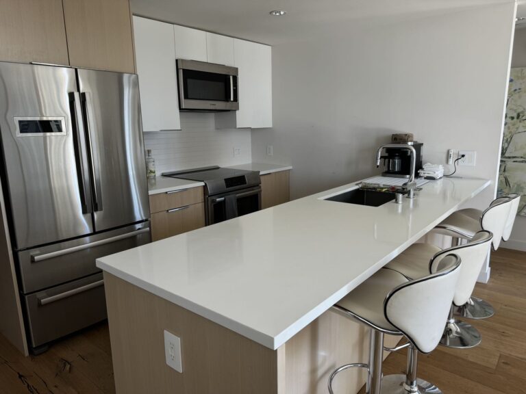 Modern kitchen with stainless steel appliances, oversized white quartz island, bar seating, and contemporary finishes.