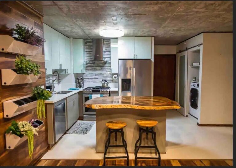 Modern kitchen with stainless steel appliances, custom wood island seating, decorative wood accent wall, and in-unit laundry.