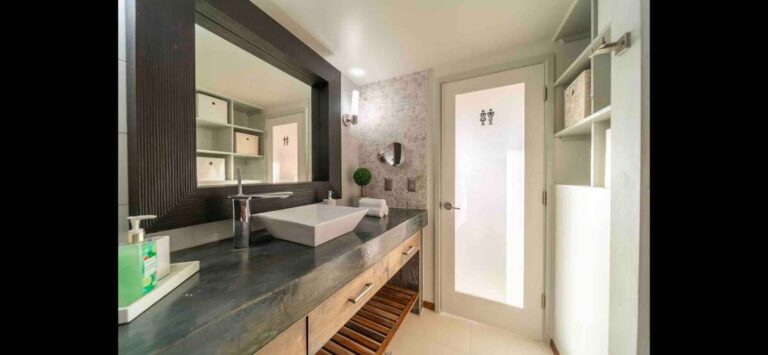 Modern bathroom with a vessel sink, oversized framed mirror, stone countertop, custom shelving, and contemporary finishes.