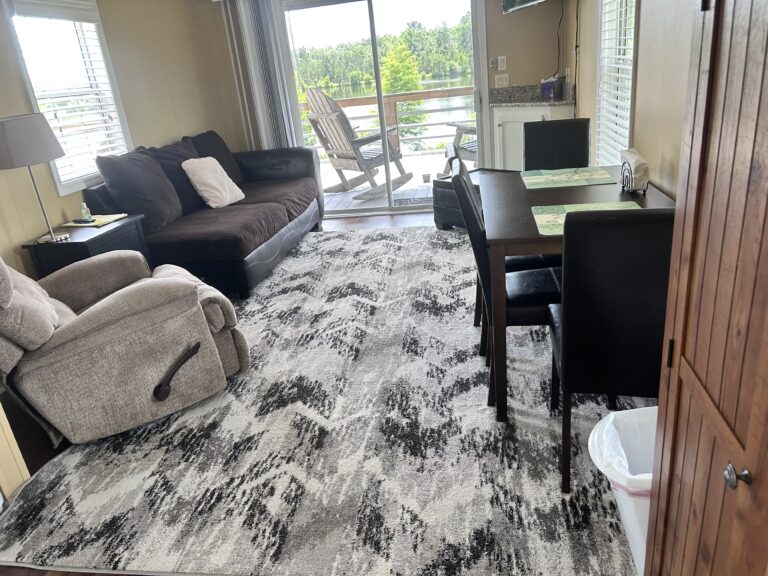 Cozy living and dining area featuring comfortable seating, a dining table for four, and sliding glass doors opening to a private deck with lake views.