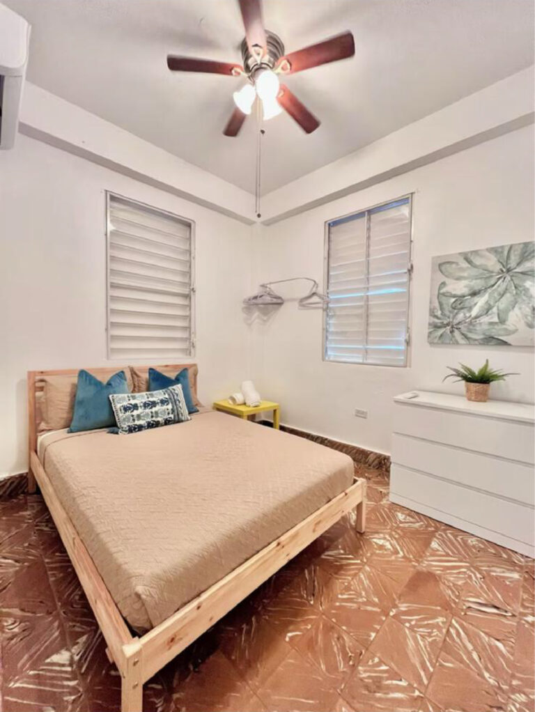 Cozy Puerto Rico bedroom with a platform bed, dresser, ceiling fan, and louvered windows.