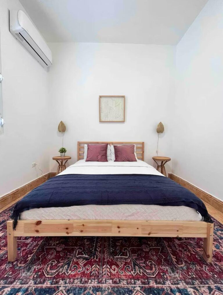Minimalist Puerto Rico bedroom featuring a platform bed, decorative area rug, bedside tables, and mini-split air conditioning.