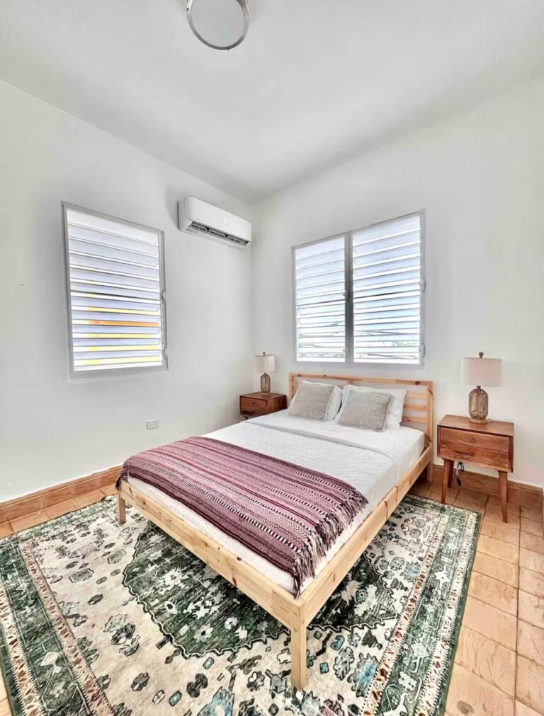 Bright Puerto Rico bedroom with a platform bed, decorative area rug, louvered windows, and mini-split air conditioning.
