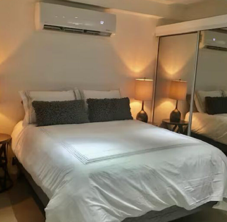 Comfortable Puerto Rico bedroom featuring a queen bed, mirrored closet doors, bedside lighting, and ductless air conditioning.