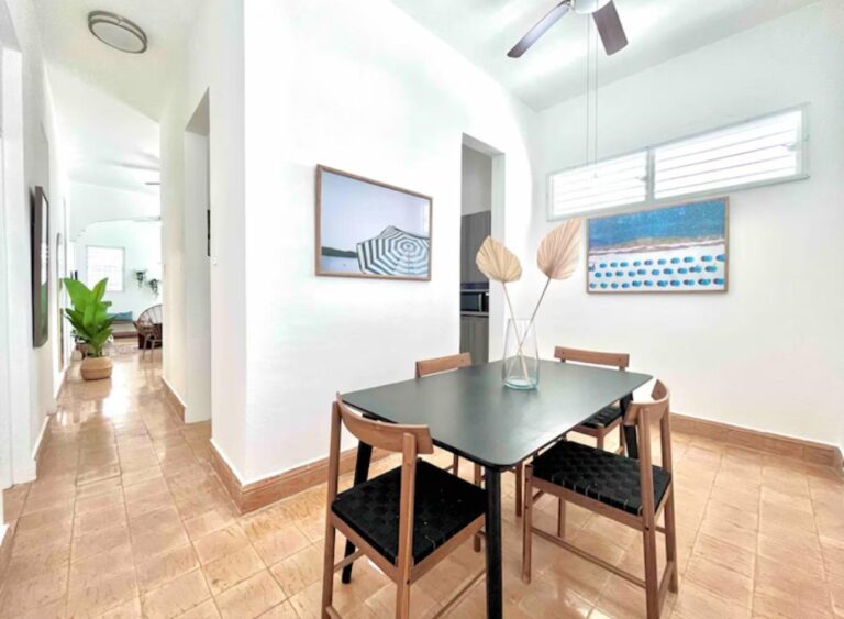 Contemporary dining room in a Puerto Rico residence featuring seating for four, coastal artwork, and abundant natural light.