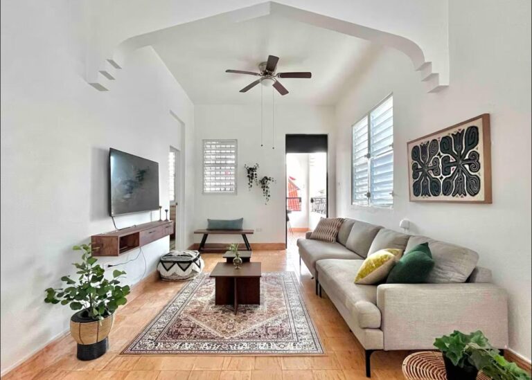 Bright furnished living room in Puerto Rico featuring high ceilings, comfortable sofa, smart TV, decorative furnishings, ceiling fan, and access to a private balcony.