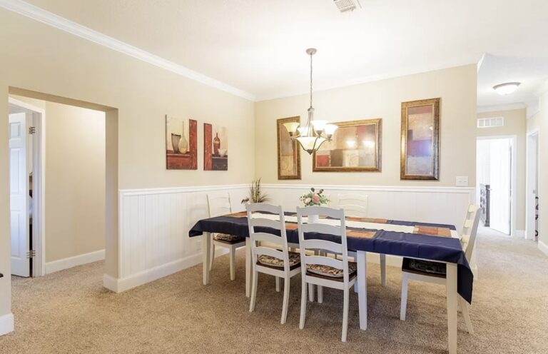Formal dining room featuring a six-seat dining table, decorative lighting fixture, elegant wall accents, and an open layout connecting to the main living areas.