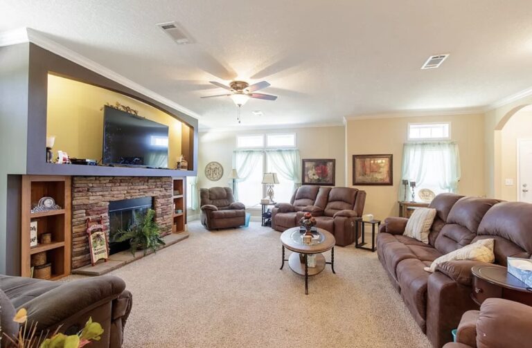 Large family room with plush reclining sofas, stone fireplace, mounted television, and bright natural light.