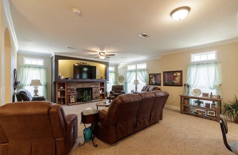 Spacious living room with reclining seating, stone fireplace, large television, and abundant natural light.