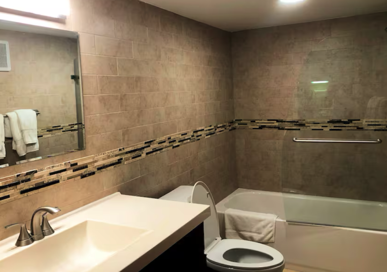 Updated bathroom with modern vanity, tiled tub-shower combination, glass enclosure, and contemporary finishes.