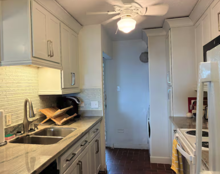 Updated galley kitchen with custom cabinetry, stone countertops, stainless sink, and full-size appliances.