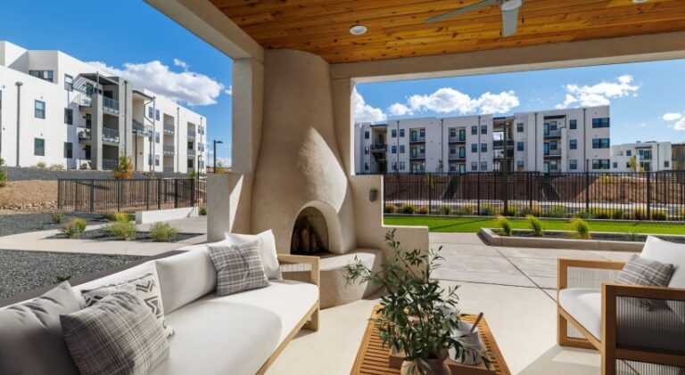 Covered outdoor lounge at Solwyn Santa Fe featuring comfortable seating, a built-in fireplace, landscaped courtyard, and modern apartment buildings.